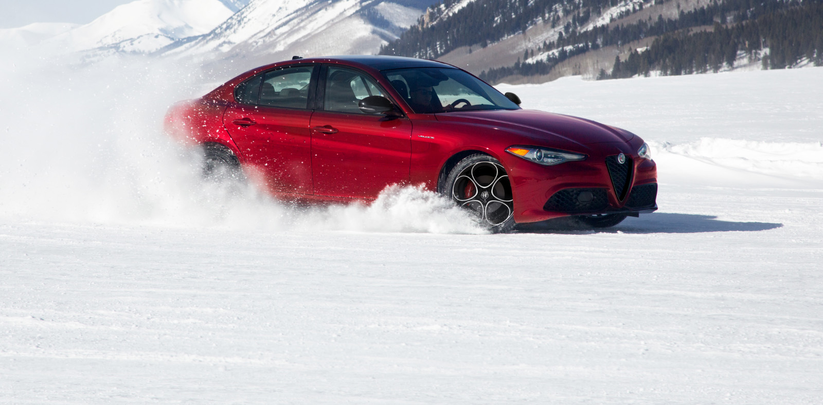Un Alfa Romeo Giulia Veloce 2023 rojo levantando nieve mientras recorre las montañas.