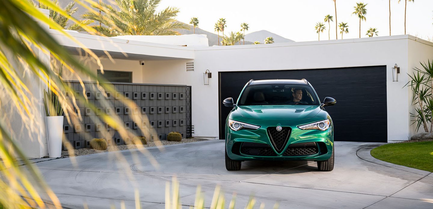 Se muestra una vista frontal de un Alfa Romeo Stelvio Veloce 2023 verde estacionado en la entrada para automóviles de una casa contemporánea.