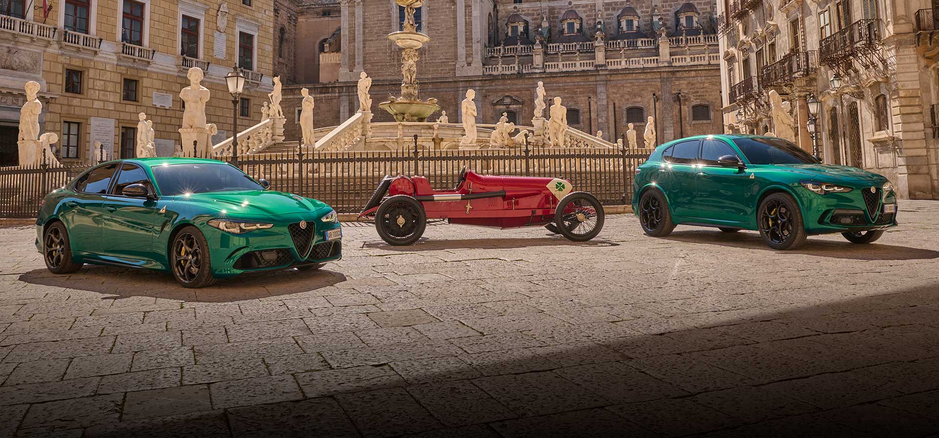 Tres vehículos Alfa Romeo Quadrifoglio estacionados en un patio rodeado de arquitectura renacentista. De izquierda a derecha: un Alfa Romeo Giulia Quadrifoglio 2024 verde, un auto de carrera Alfa Romeo Quadrifoglio clásico rojo y un Alfa Romeo Stelvio Quadrifoglio 2024 verde.