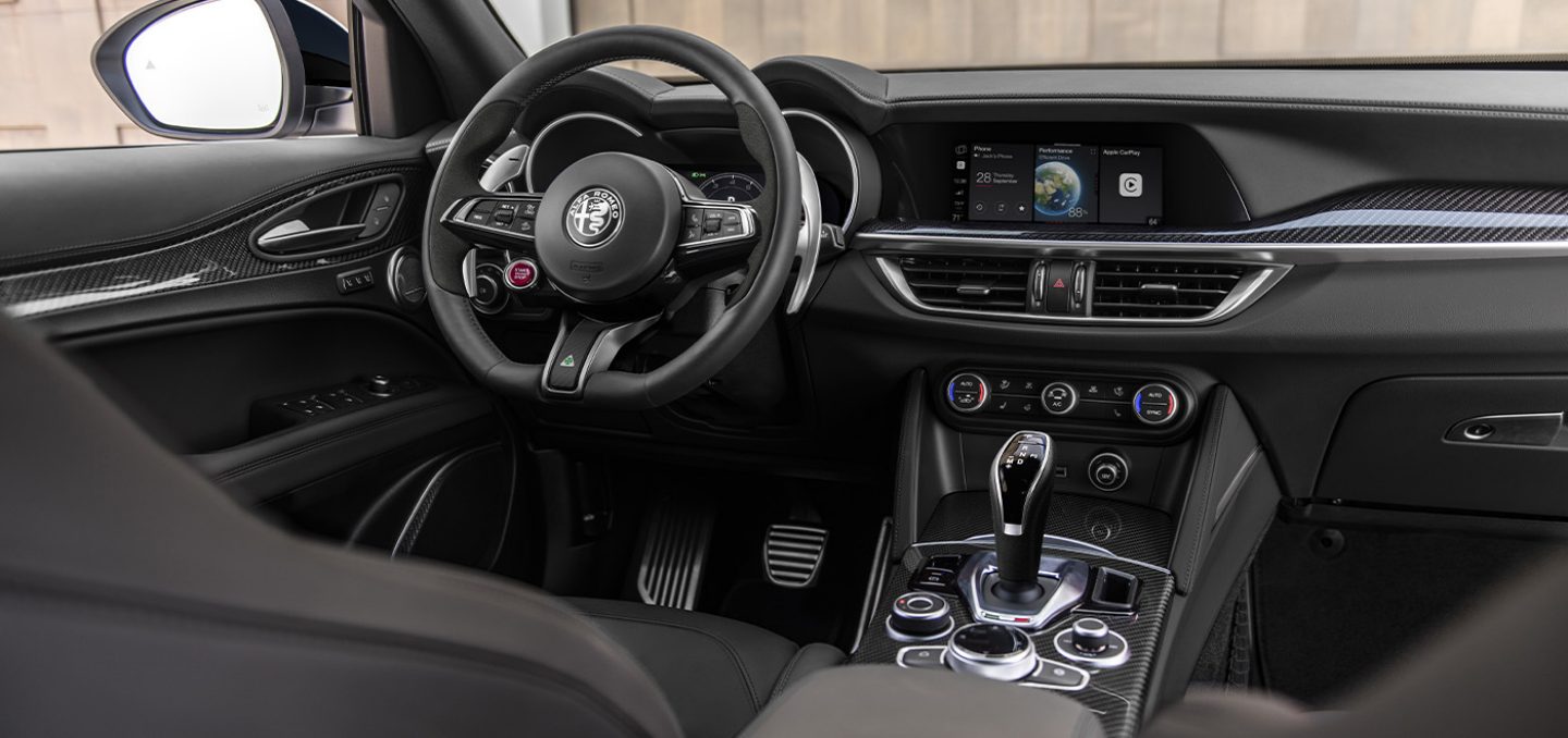 Mostrar El interior del Alfa Romeo Stelvio TBD 2024 con foco en el volante, la consola central y la pantalla multitáctil.