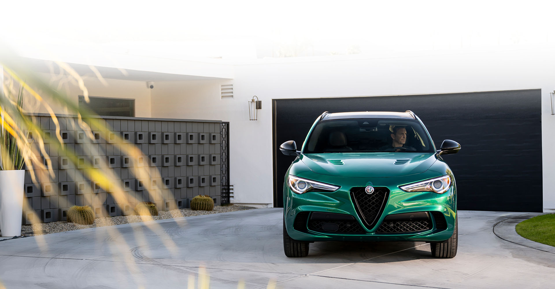 Un Alfa Romeo Stelvio Quadrifoglio 2023 verde estacionado en la entrada para automóviles de una casa moderna, con un conductor en el interior.